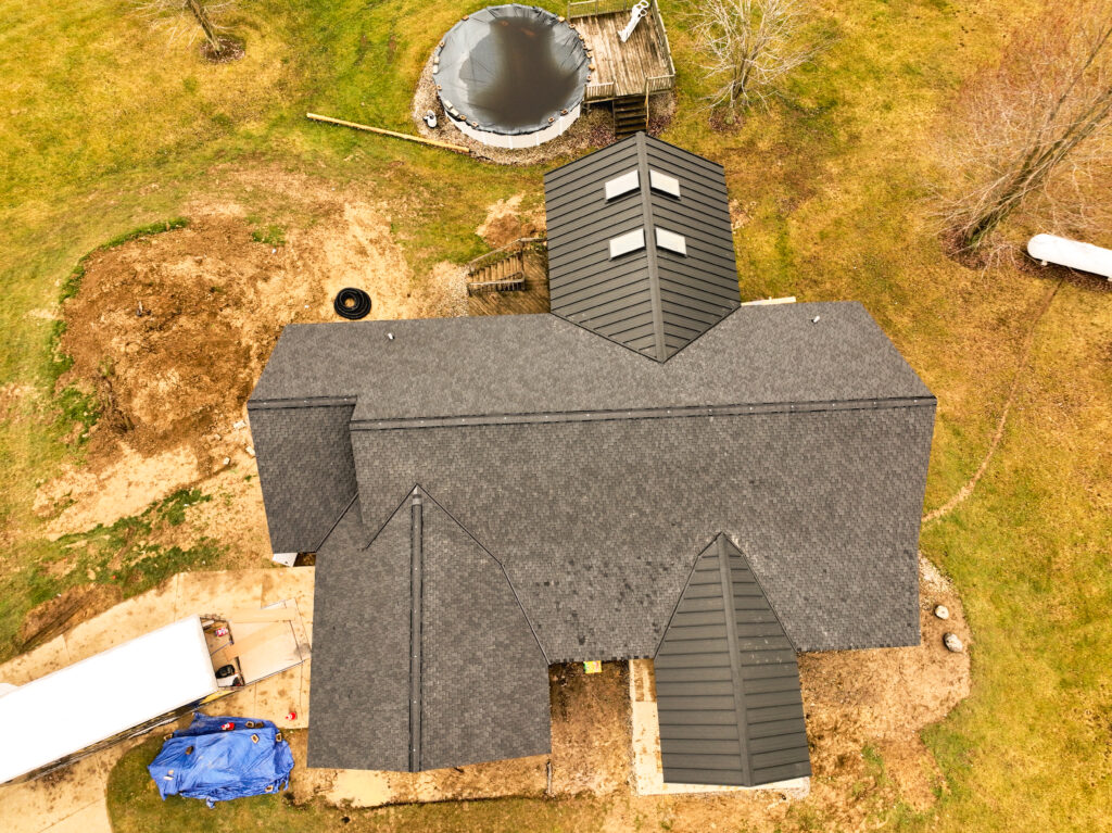 Overhead view of a gray shingle roof with dark metal roofing over the front and rear porches
