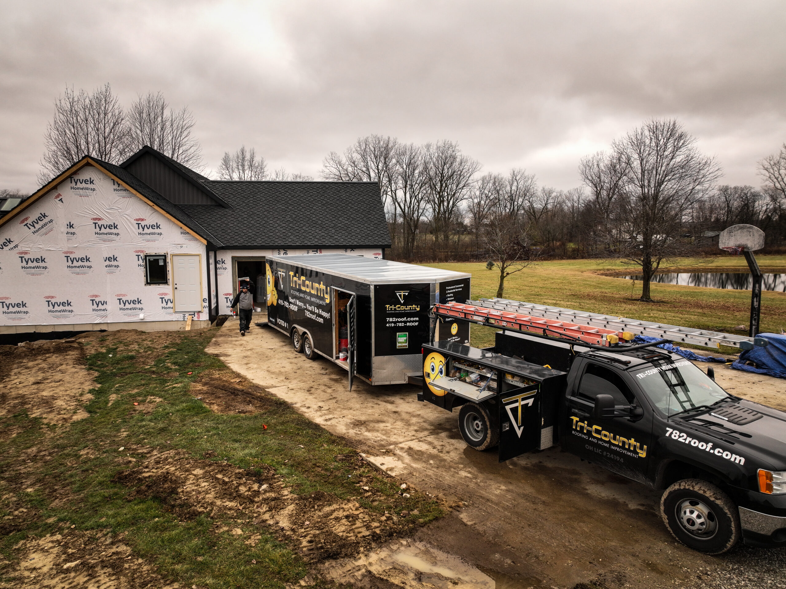 Tri-County work truck and equipment trailer beside a house under construction